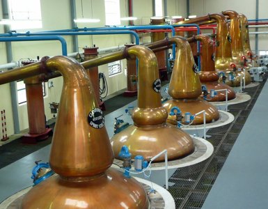 Crerar Group | A row of large, gleaming copper pot stills inside a bright Scotch whisky distillery, used for the distillation process. ?? Crerar Group